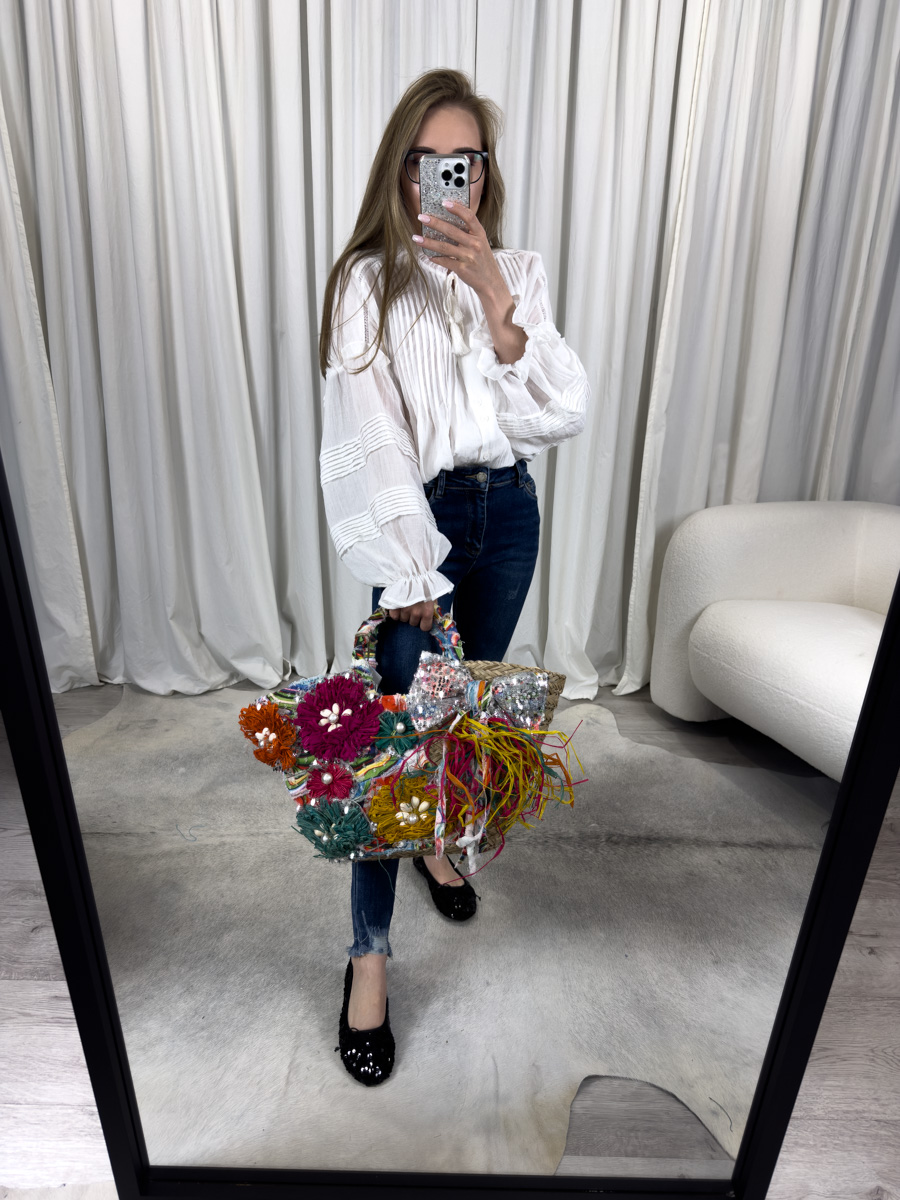 koszula-boho-biala-wiya-3 Zdjęcie produktowe sklepu internetowego z odzieżą damską – modelka ubrana w koszule Boho białą marki Wiya i jeansowe spodnie, trzymająca torebkę wiklinową w ręce